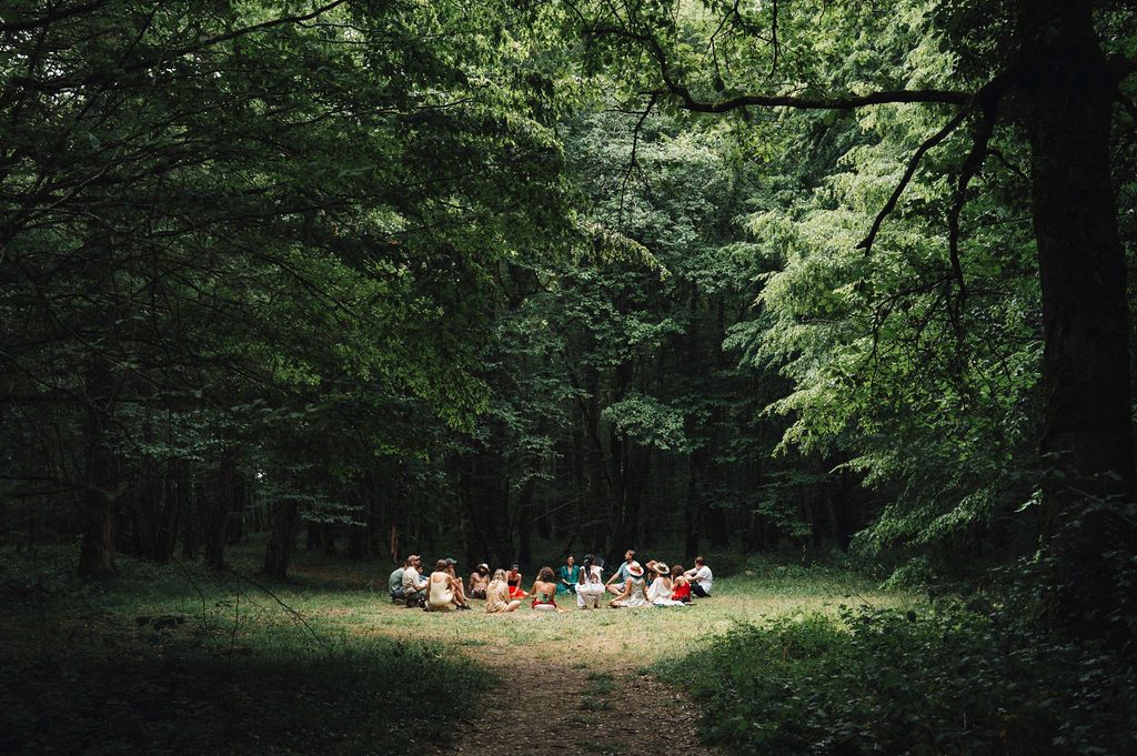 A circle of people in conversation in a forest clearing at ma/ré